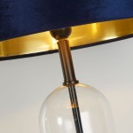 Czarna i granatowa lampa stołowa Oxford z abażurem z weluru i złotym wnętrzem. Widoczny przezroczysty klosz, metalowa nóżka w kolorze brązu. Lampa ma miejsce na żarówkę E27. Ujęcie zbliżeniowe na detal konstrukcji.