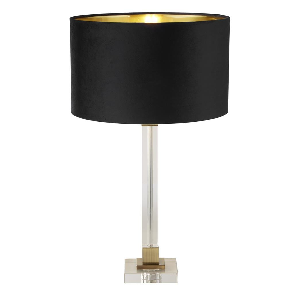 Lampa stołowa Scarborough z mosiężnymi akcentami i czarnym, teksturowanym abażurem. Ustawiona na przezroczystym, prostokątnym postumencie. Abażur ma złote wnętrze, co podkreśla elegancki wygląd lampy.