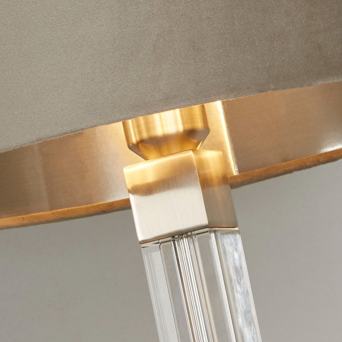 Lampa stołowa Scarborough z kloszem w kolorze taupe, wykończona satynowym niklem. Widoczny detal podstawy z przezroczystego szkła i metalowych akcentów, tworzący elegancki wygląd. Kąt ujęcia zbliżenie na połączenie klosza z podstawą.