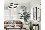 Lampa wisząca Cornelia 2xLED/60W w kolorze czarnym, o nowoczesnym, spiralnym kształcie. Zawieszona w jasnym wnętrzu z roślinnością i sofą, tworzy elegancką aranżację. Widoczne detale to białe elementy dekoracyjne oraz stylowe poduszki na kanapie.