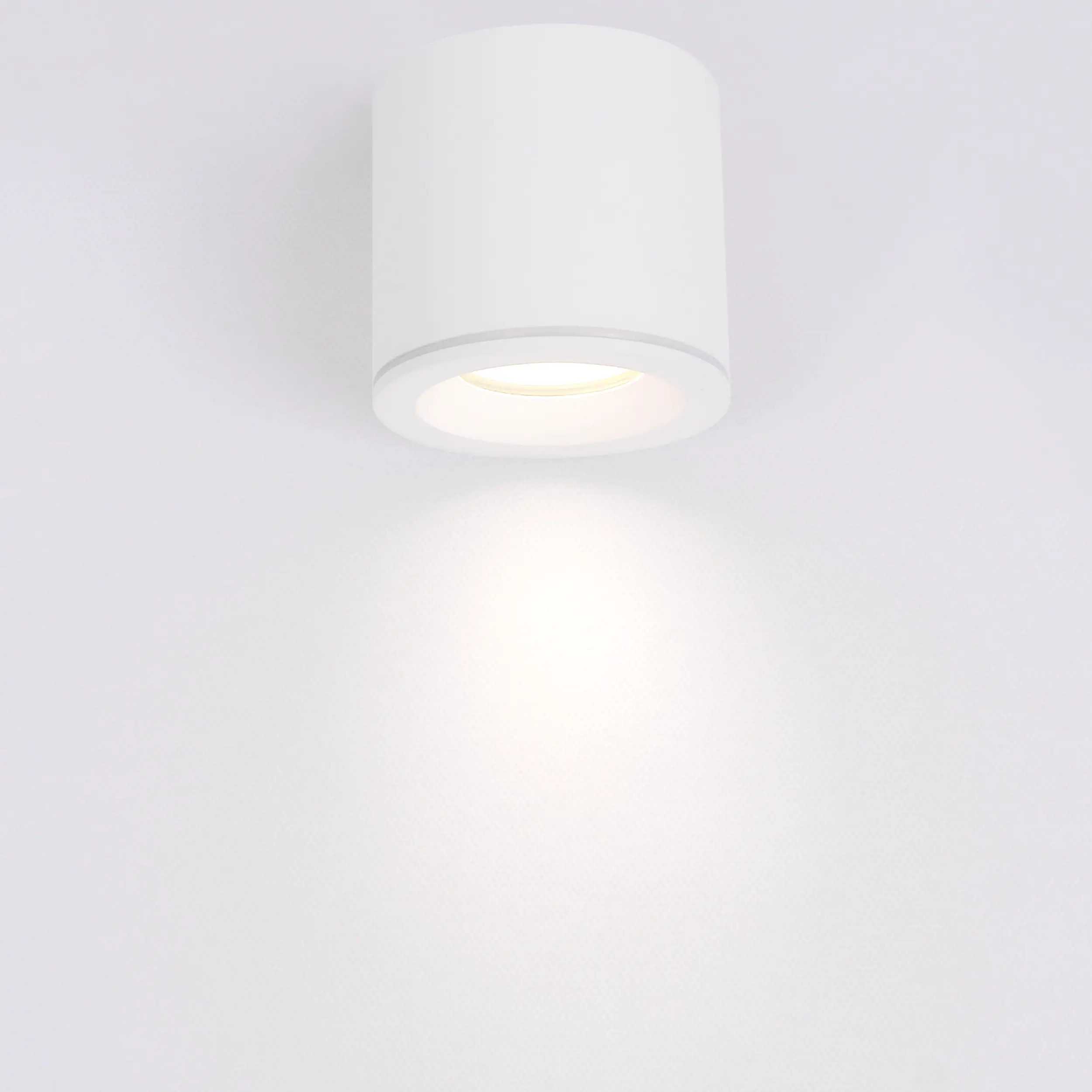 Biała lampa sufitowa w formie tuby z oprawą na żarówkę GU10, zamontowana na gładkim tle. Okrągły kształt z delikatnym wykończeniem, emitująca jasne światło. Idealna do oświetlenia wnętrz, z klasą szczelności IP65.