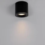 Czarna lampa sufitowa tuba Luna z miejscem na żarówkę GU10, o stopniu ochrony IP65. Ujęcie frontalne, lampa montowana do sufitu, emitująca światło na jasne tło. Prosta, cylindryczna forma z widocznym źródłem światła.