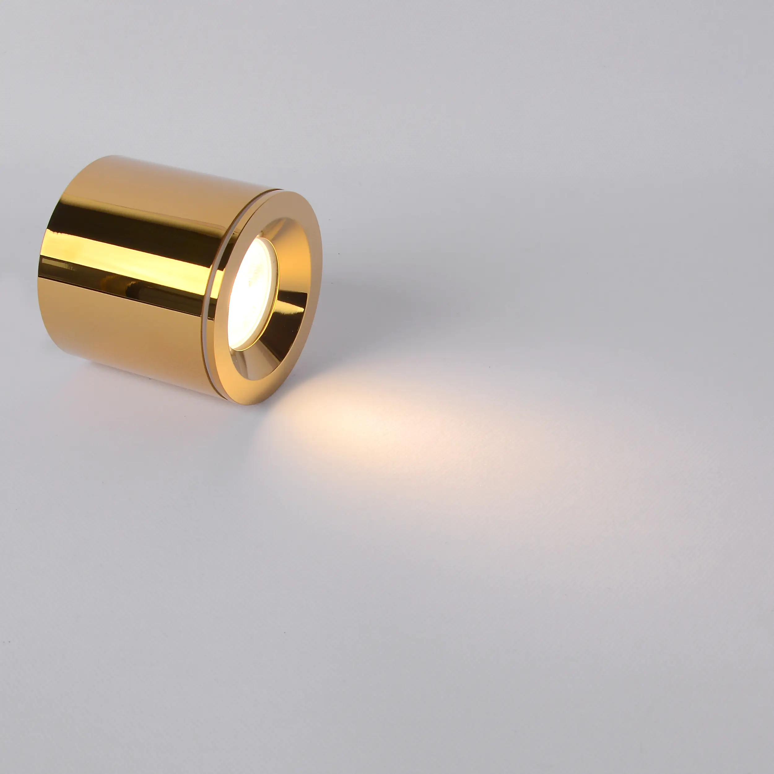 Złota lampa sufitowa tuba Luna, z oprawą 1xGU10, o matowej powierzchni i cylindrycznym kształcie, ustawiona na białym tle. Emituje jasne światło, z widoczną soczewką wewnętrzną. Idealna do nowoczesnych wnętrz.