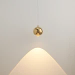 Lampa wisząca Aurenia w kolorze złotym, z oprawą w kształcie kuli. Zawieszona na cienkim przewodzie, emituje ciepłe światło, tworząc subtelny efekt na ścianie. Idealna do nowoczesnych wnętrz.
