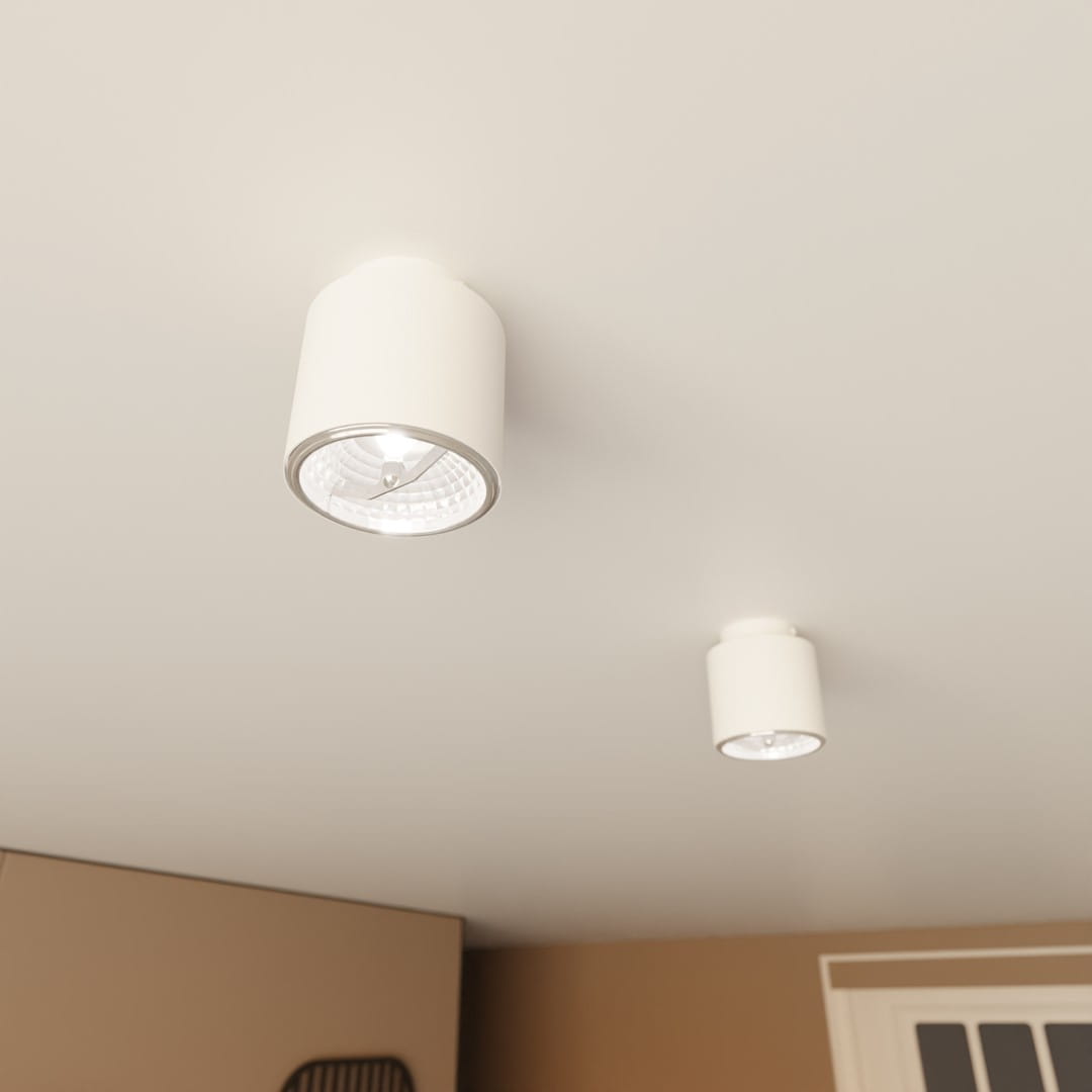 Nano lampa sufitowa 1xGU10/AR 111 w kolorze białym, okrągła obudowa z metalicznym detalem. Zamontowana na suficie, w zbliżeniu na źródło światła. W tle widoczna jasna ściana oraz fragment wnętrza.