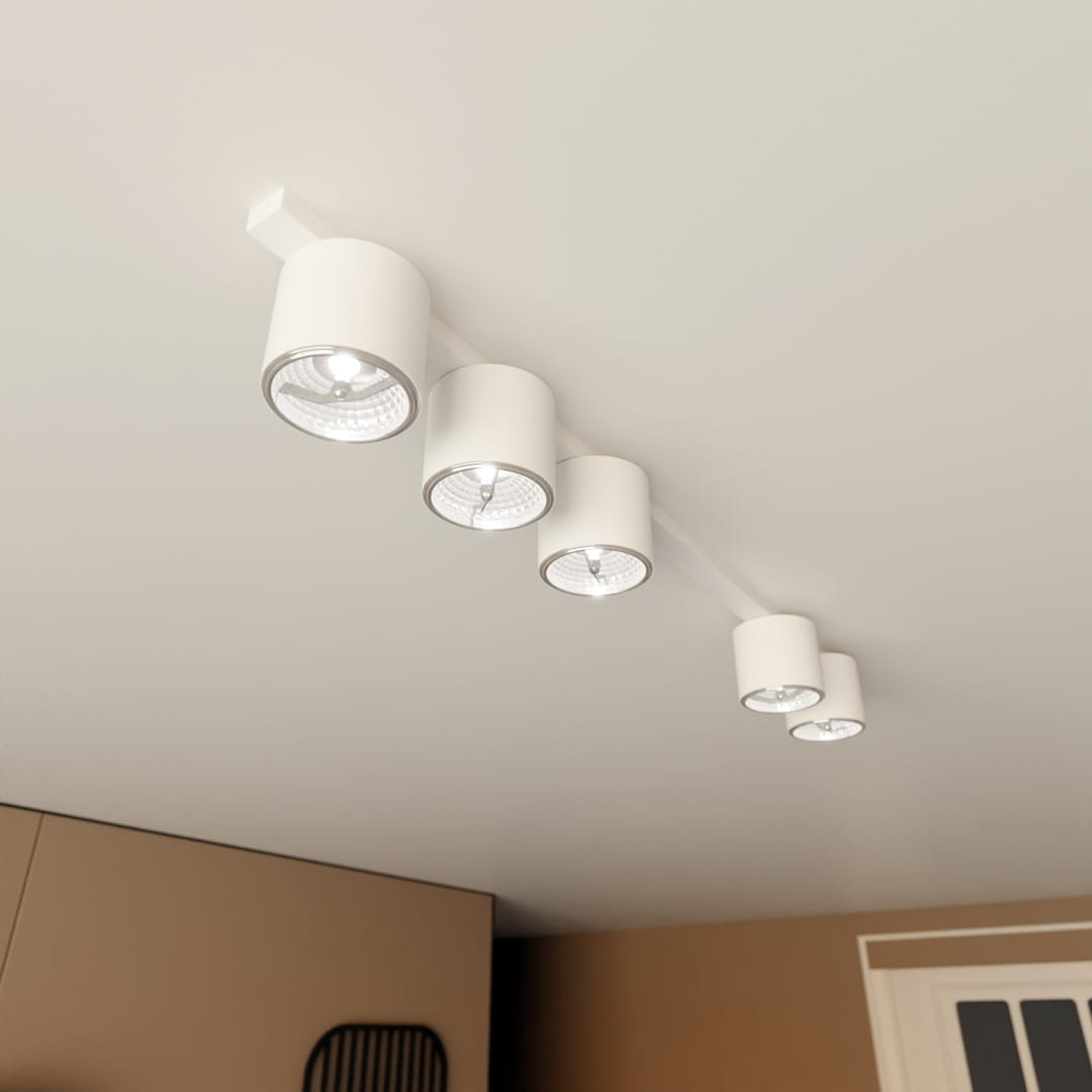Biała lampa sufitowa z pięcioma oprawami GU10, zamontowana na prostokątnej listwie. Każda oprawa ma cylindryczny kształt z metalowym wykończeniem, skierowane w dół. Lampa umieszczona na jasnym tle, w minimalistycznym wnętrzu.