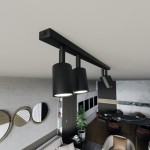 Czarna lampa sufitowa Flash z czterema spotami GU10, zamontowana na prostokątnej listwie. Widok z góry, w tle nowoczesne wnętrze mieszkania z dekoracyjnymi lustrami i rośliną. Lampy mają cylindryczny kształt i matowe wykończenie.