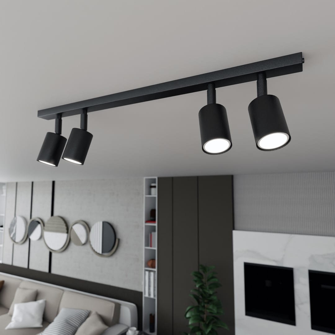 Czarna lampa sufitowa Flash z czterema reflektorami GU10, zamontowana na poziomej listwie. Reflektory mają cylindryczny kształt i emitują białe światło. Lampa umieszczona w nowoczesnym wnętrzu z sofą i dekoracyjnymi lustrami w tle.