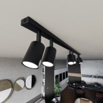 Czarna lampa sufitowa (spot) z sześcioma oprawami na żarówki GU10, zamontowana na prostokątnej listwie. Ujęcie z góry, ukazujące stylowe, cylindryczne klosze oraz nowoczesne wnętrze z elementami dekoracyjnymi w tle.