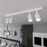 Biała lampa sufitowa typu spot z czterema oprawami GU10, zamontowana na prostokątnej listwie. Ujęcie z góry, pokazujące trzy skierowane w dół reflektory, w nowoczesnym wnętrzu z szaro-białym tłem oraz rośliną.
