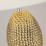 Lampa stołowa Nadine z żółtą, teksturowaną podstawą w kształcie owalnym. Wykończenie w kolorze złotym, z kremowym kloszem na górze. Ujęcie z bliska, podkreślające detale struktury podstawy.