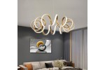 Lampa wisząca Loop w kolorze złotym z pilotem, posiadająca unikalny, falisty kształt. Wykonana z materiałów LED, emitująca ciepłe światło. Zawieszona w nowoczesnym wnętrzu, na tle szarej ściany i zasłon.