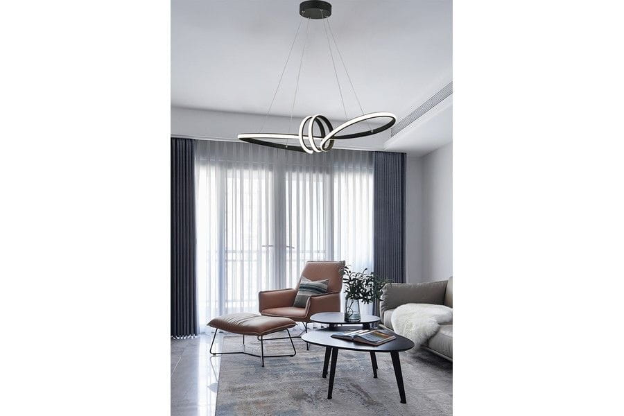 Czarna lampa wisząca Canbera z jedną diodą LED 40W, o nowoczesnym, minimalisticznym kształcie z płynnymi liniami. Zawieszona na cienkich linkach, w aranżacji nowoczesnego wnętrza z brązowym fotelem i okrągłym stołem.