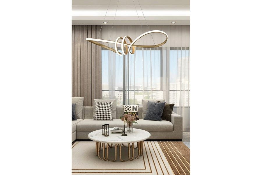 Lampa wisząca Canbera z jedną żarówką LED 40W w kolorze złotym. Ma nowoczesny, organiczny kształt, zawieszona nad okrągłym stołem w jasnym wnętrzu salonu z szarymi zasłonami i sofą. W tle widoczne dekoracyjne poduszki i stół kawowy.