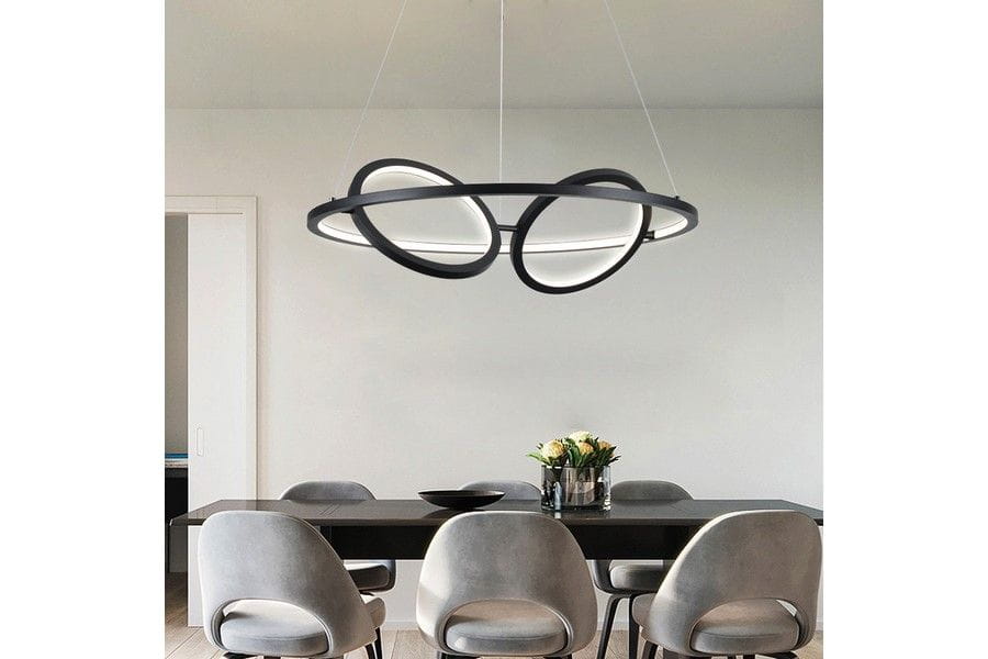 Czarna lampa wisząca Gilian z trzema źródłami LED 40W, o nowoczesnym, owalnym kształcie, zawieszona nad stołem w jadalni. W tle widoczna drewniana ściana oraz szare krzesła. Lampa ma subtelną, matową powierzchnię.