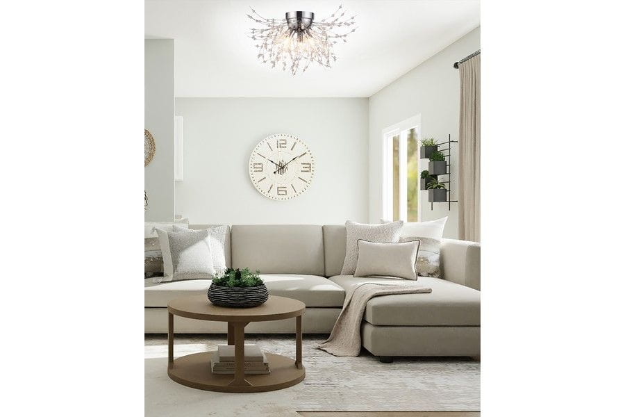 Lampa sufitowa Pearls w kolorze chromu, z trzema źródłami światła G9, umieszczona w nowoczesnym wnętrzu. Kąt ujęcia z góry, ukazujący lampa i jasne ściany. W tle sofa, zegar ścienny oraz rośliny w dekoracyjnych donicach.