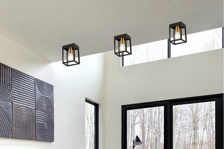 Cage lampa sufitowa 1xE27 w kolorze czarnym z mosiężnymi detalami, zawieszona na białym suficie. Widoczna w nowoczesnym wnętrzu z dużymi oknami oraz dekoracyjną ścianą z reliefami.