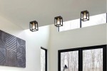 Cage lampa sufitowa 1xE27 w kolorze czarnym z mosiężnymi detalami, zawieszona na białym suficie. Widoczna w nowoczesnym wnętrzu z dużymi oknami oraz dekoracyjną ścianą z reliefami.