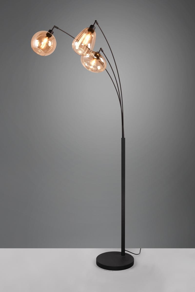 Lampa podłogowa Lumina 3xE14 w kolorze czarnym z bursztynowymi kloszami. Stojąca konstrukcja z trzema elastycznymi ramionami, które zakończone są okrągłymi i owalnymi kloszami. Podstawa okrągła, stabilna. Tło szare.