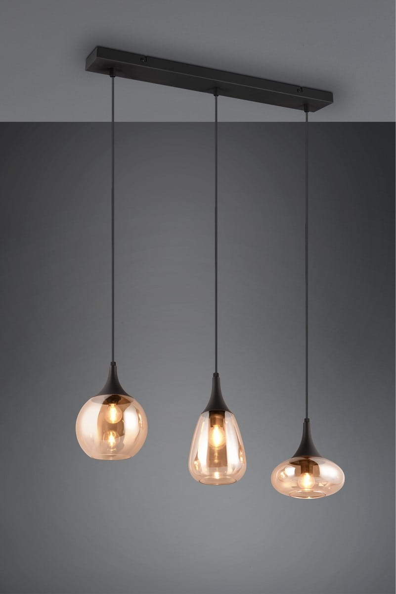 Lampa wisząca Lumina z trzema kloszami E14 w kształcie kropli, w kolorze czarnym z bursztynowym wykończeniem. Klosze zawieszone na cienkich linkach, mocowane do prostokątnej, czarnej podstawy. Tło w odcieniach szarości.