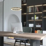 Złota lampa wisząca Aurum D60 z jednym źródłem LED o mocy 27W, okrągła, zawieszona nad drewnianym biurkiem. W tle widoczna nowoczesna biblioteka z książkami oraz dekoracyjnymi elementami.