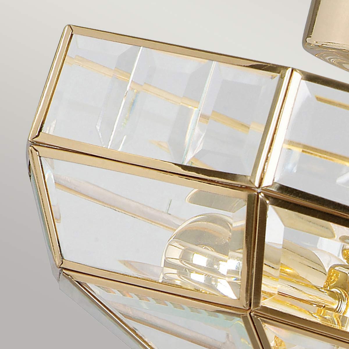 Lampa sufitowa Old Park z polerowanego mosiądzu, z dwoma oprawami E27. Elementy szklane w geometrycznym kształcie, odbijające światło. Ujęcie zbliżeniowe, ukazujące szczegóły konstrukcji i przezroczystość materiału.