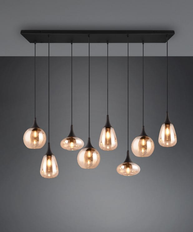 Lampa wisząca Lumina 8xE14 w czarnej obudowie z bursztynowymi kloszami, zawieszona na długich przewodach, z różnymi kształtami kloszy. Montowana do sufitu, w minimalistycznym stylu, na ciemnym tle.