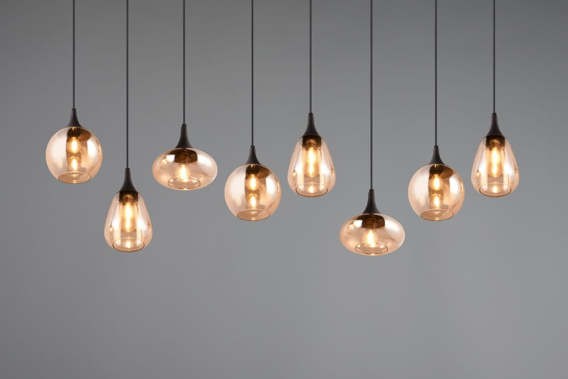 Lampa wisząca Lumina z 8 kloszami E14 w kolorze czarnym i bursztynowym. Klosze mają różne kształty, zawieszone na cienkich linkach, tworząc asymetryczny układ. Tło jest szare, co podkreśla elegancję lampy.