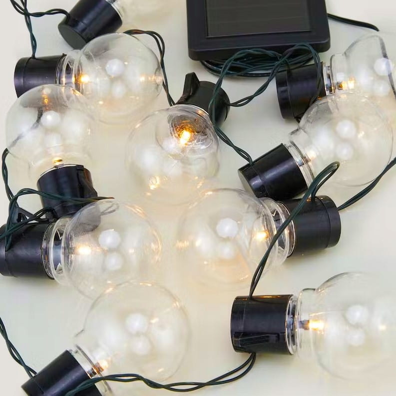 Girlanda ogrodowa solarna z 30 kulkami LED w czarnych oprawkach, długość 7,7 m. Kule mają przezroczyste, okrągłe klosze z widocznymi diodami, a zasilanie pochodzi z panelu słonecznego. Kabel w kolorze ciemnozielonym.
