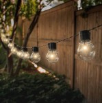 Girlanda ogrodowa solarna z 30 kulkami LED, długość 7,7 m, z czarnym przewodem. Kule LED w kształcie żarówek zawieszone w równych odstępach, otoczone zielenią, w tle drewniana ogrodzenie.