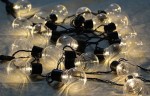 Girlanda ogrodowa solarna z 30 kulkami LED o długości 7,7 m, z czarnym przewodem. Kule LED w transparentnym kloszu emitują ciepłe światło, ułożone w nieregularny sposób, idealne do dekoracji przestrzeni zewnętrznych.
