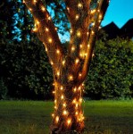 Girlanda świetlna ogrodowa solarna z 200 diodami LED, o długości 20 m, owinięta wokół pnia drzewa. Ciepłe białe światło, widoczna struktura przewodów. Urokliwy element dekoracyjny, idealny do aranżacji ogrodów.