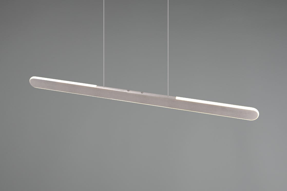 Lampa wisząca Helios w kolorze aluminium z jedną diodą LED o mocy 28W. Posiada prostokątny, smukły kształt z zaokrąglonymi końcami, zawieszona na cienkich linkach, o minimalistycznym designie. Tło szare, jednolite.