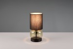 Lampa stołowa Elio, z kloszem w kolorze czarnym i podstawą z zielonego szkła, stojąca na okrągłej, ciemnej podstawie. Klosz wykonany z materiału tekstylnego, emitujący ciepłe światło. Ujęcie frontalne, na jednolitym tle.