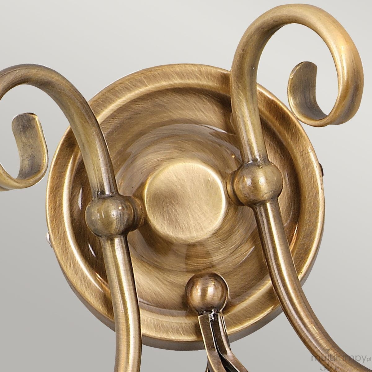 Kinkiet Artisan 2xE14 w postarzanym mosiądzu, z dekoracyjnymi, spiralnymi ramionami. Widoczny detal mocowania oraz tekstura metalu. Ujęcie z bliska, pokazujące stylowy design i kolor.