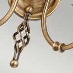 Kinkiet Artisan w kolorze postarzanym mosiądzu z dwoma gniazdami E14. Widoczna spiralna dekoracja oraz kulisty element na końcu. Produkt zamontowany na okrągłej podstawie, z delikatnymi, metalowymi ramionami. Tło jasne, jednolite.