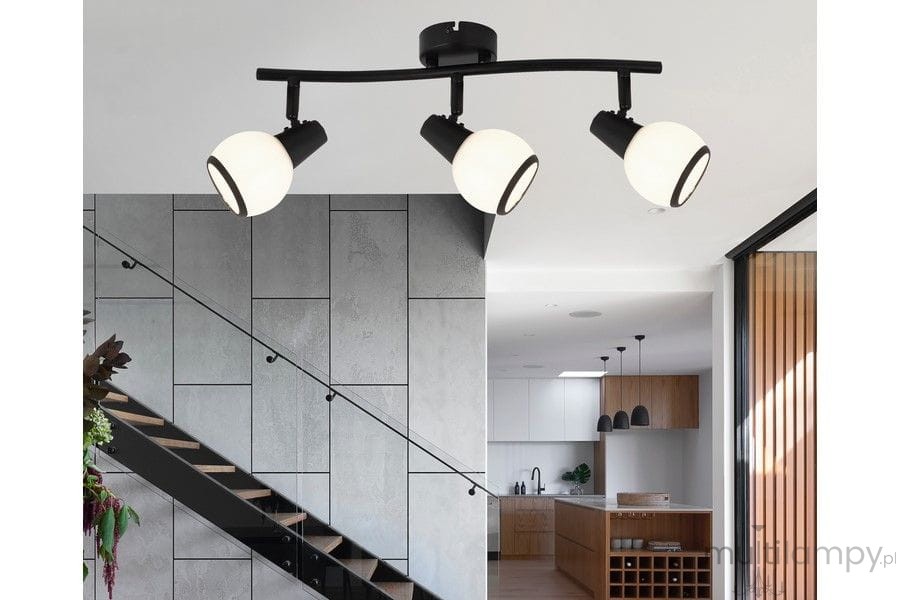 Czarna lampa sufitowa Loris z trzema reflektorami E14. Okrągłe, matowe klosze w białym kolorze, zamontowane na łukowatej, czarnej oprawie. Lampa umieszczona w nowoczesnym wnętrzu, nad schodami, z widokiem na kuchnię w tle.