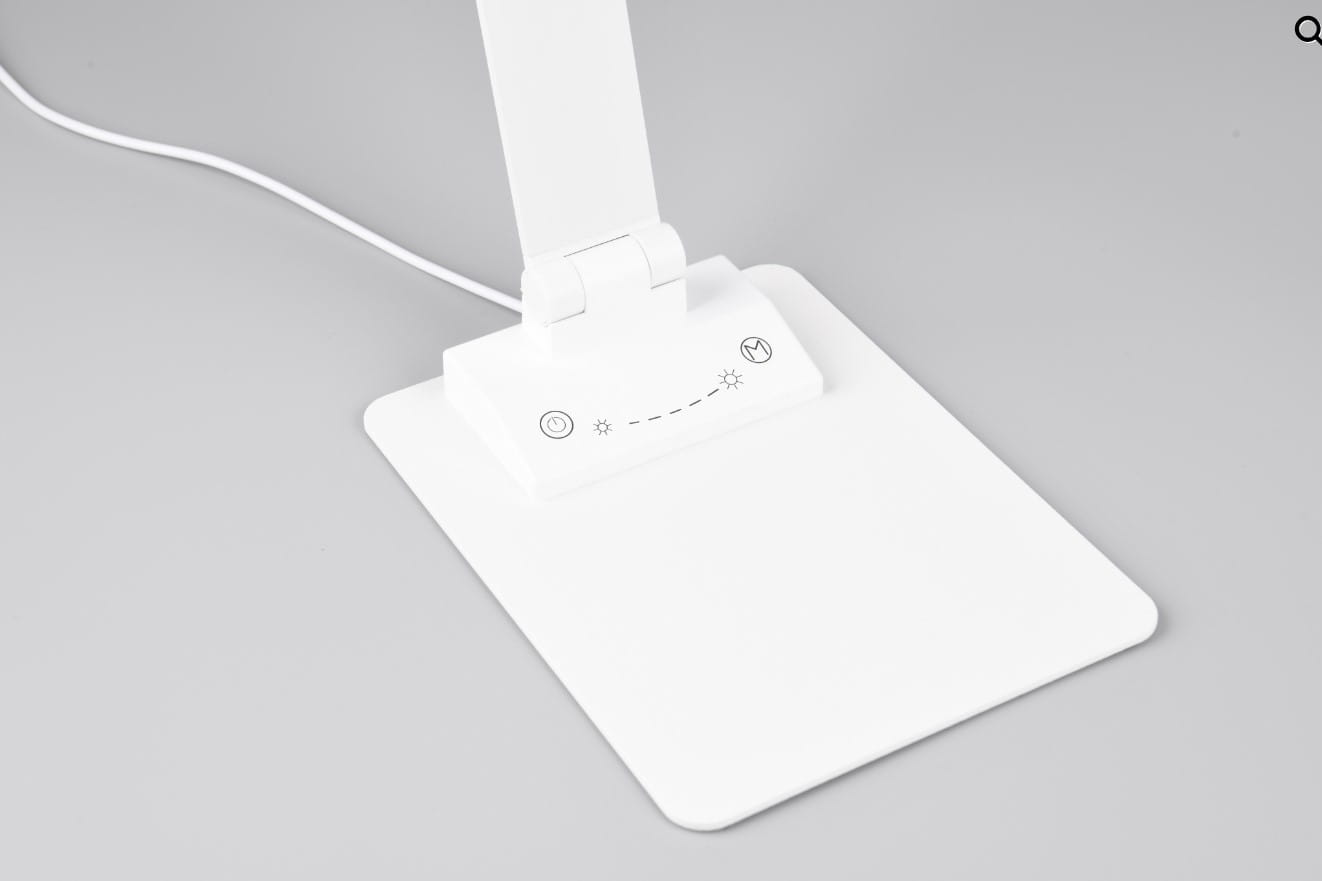 Lampka biurkowa Travis w kolorze białym z portem USB-C, posiadająca zintegrowany moduł LED o mocy 6,5W. Ujęcie z boku, ukazuje podstawę z przyciskami do regulacji jasności oraz włączania/wyłączania. Prosta, nowoczesna konstrukcja.