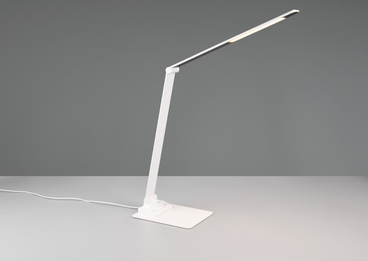 Lampka biurkowa Travis w kolorze białym, z elastycznym ramieniem i płaską podstawą. Posiada wbudowany port USB-C, źródło światła LED o mocy 6,5W. Ujęcie z boku, ukazujące nowoczesny design i funkcjonalność. Kabel zasilający widoczny na stole.