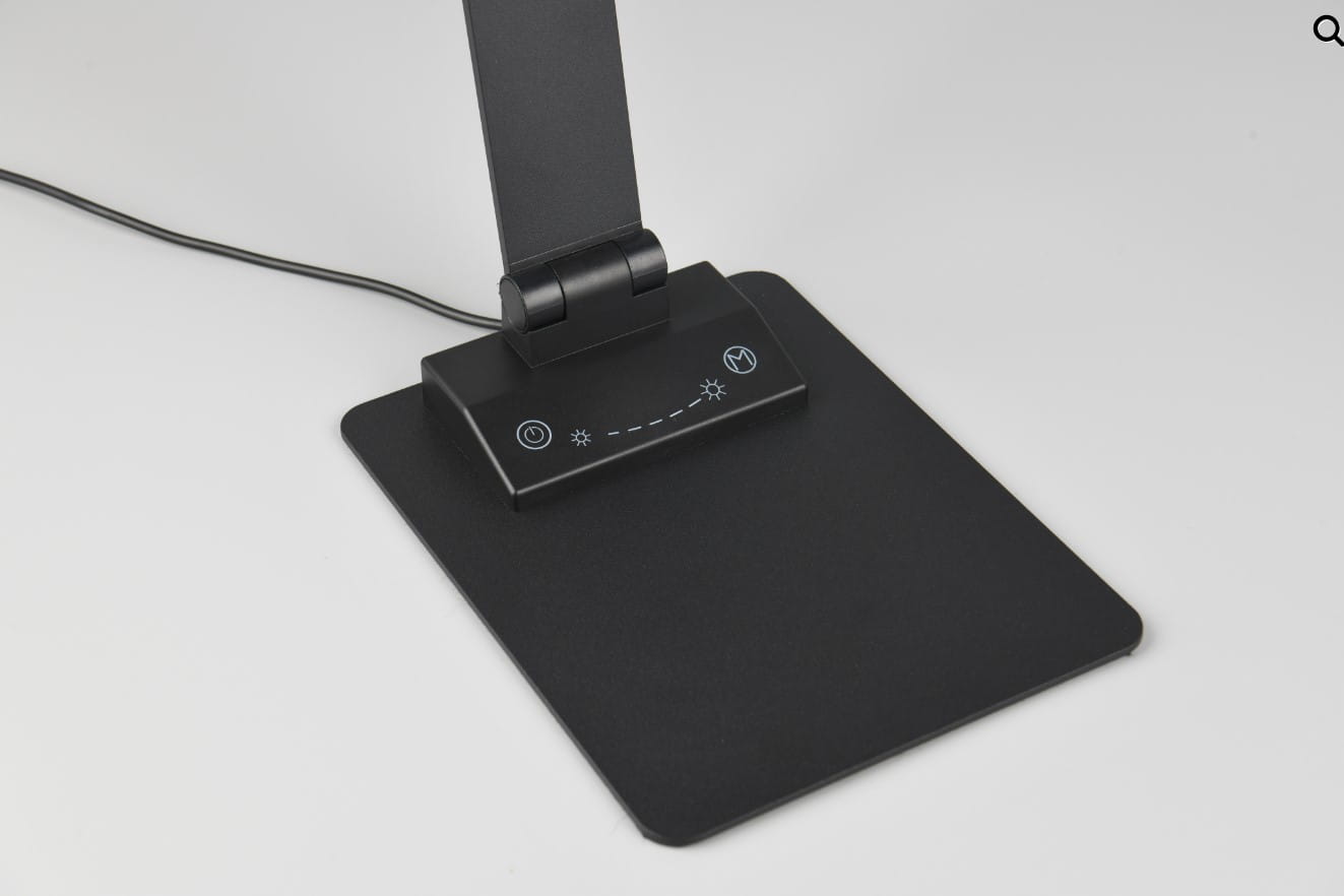 Lampka biurkowa Travis w kolorze czarnym z portem USB-C. Posiada prostokątną podstawę z dotykowym panelem sterowania, zawierającym przycisk zasilania oraz regulację jasności. Kąt ujęcia ukazuje dolną część lampy i jej detale.