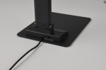 Czarna lampka biurkowa Travis z portem USB-C, wykonana z materiału matowego, z prostokątną podstawą. Widoczne dwa porty USB oraz kabel zasilający. Ujęcie z boku, prezentujące detale w dolnej części lampki.
