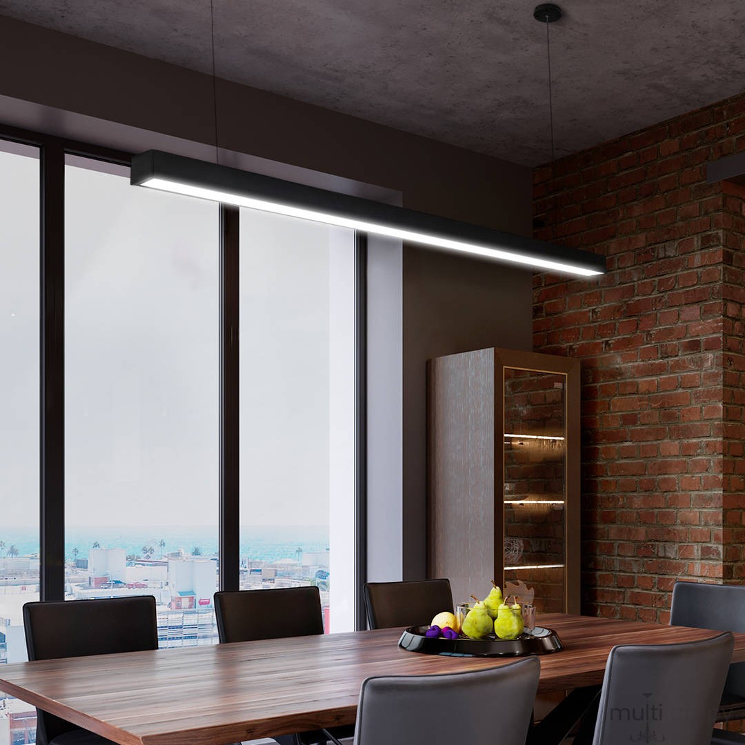 Lampa wisząca Linia w kolorze czarnym, z jednym źródłem LED o mocy 40W i temperaturze barwowej 3000K, zamontowana nad drewnianym stołem w nowoczesnym wnętrzu z widokiem na miasto, na tle ściany z cegły.