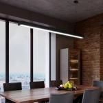 Lampa wisząca Linia w kolorze czarnym, z jednym źródłem LED o mocy 40W i temperaturze barwowej 3000K, zamontowana nad drewnianym stołem w nowoczesnym wnętrzu z widokiem na miasto, na tle ściany z cegły.