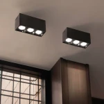 Lampa sufitowa LED o mocy 9W w czarnej obudowie, z trzema źródłami światła. Ujęcie z dołu, pokazujące lampy zamontowane na suficie, w tle widoczna okna z drewnianymi ramami. Kolor światła 3000K zapewnia ciepłe oświetlenie.