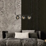 Lampa wisząca Alisa 3XE14 w kolorze grafitowym z trzema dymionymi kloszami. Produkt zawieszony nad łóżkiem w aranżacji sypialni, na tle ciemnej ściany i dekoracyjnej tapety w odcieniach szarości.