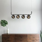 Lampa wisząca Alisa w kolorze grafitowym z czterema dymionymi kloszami. Ułożona poziomo na czarnym stelażu, zawieszona nad drewnianą komodą. W tle widoczna dekoracyjna roślina w szklanej wazonie.