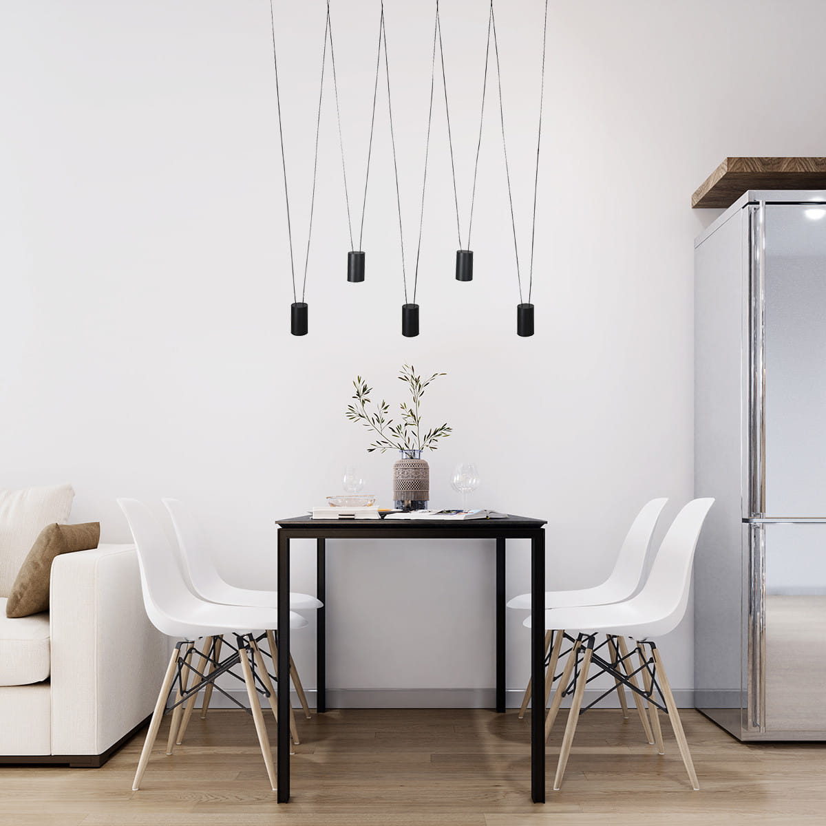 Czarna lampa wisząca Toledo z pięcioma oprawami GU10, zawieszona na cienkich linkach, nad prostokątnym stołem w jasnym wnętrzu. W tle białe krzesła i szafka, na stole wazon z gałązką.