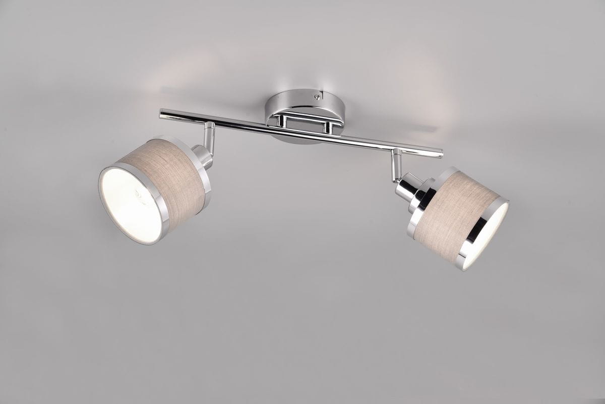 Lampa sufitowa Arosa z dwoma reflektorami w kolorze chromu. Każdy reflektor ma jasnoszary abażur z materiału. Produkt zamontowany na prostokątnej podstawie, w widoku frontalnym, z lekko nachylonymi reflektorami.