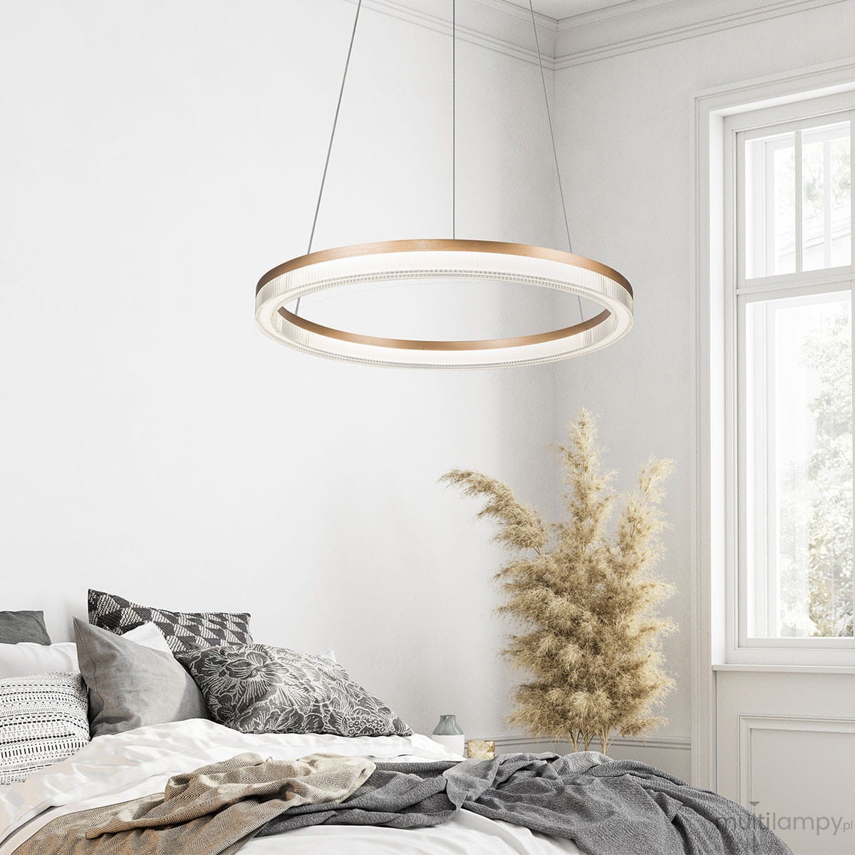 Lampa wisząca Midway Crystal D60 w złotym kolorze, okrągła, zawieszona na cienkich linkach. Wyposażona w diodę LED o mocy 40W. W tle widoczna sypialnia z poduszkami na łóżku i rośliną dekoracyjną. Tło jasne, minimalistyczne.
