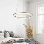 Lampa wisząca Midway Crystal D60 w złotym kolorze, okrągła, zawieszona na cienkich linkach. Wyposażona w diodę LED o mocy 40W. W tle widoczna sypialnia z poduszkami na łóżku i rośliną dekoracyjną. Tło jasne, minimalistyczne.